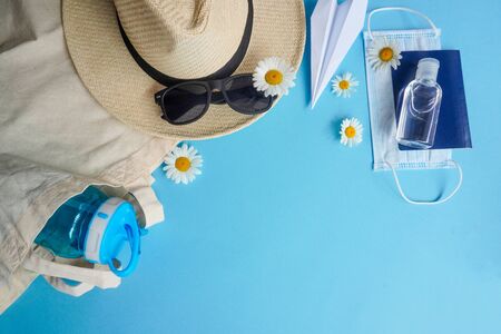 Summer layout with straw hat, daisies and sunglasses, airplane-origami, sanitizer, passport and medical mask.Concept of travel and recreation. Flights to sea, rest during coronavirus. Flatly on blueの写真素材
