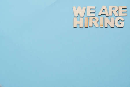 Search for employees, recruitment after crisis and coronavirus. now hiring-wooden letters on blue background. flatly with copy space, background.new hiring positions.の写真素材