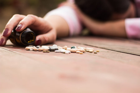 Woman taking medicine overdose and lying on the wooden table with open pills bottle