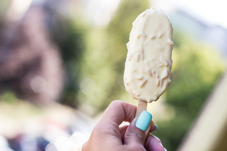 Young woman hand holding ice cream with white chocolate glaze, outdoors