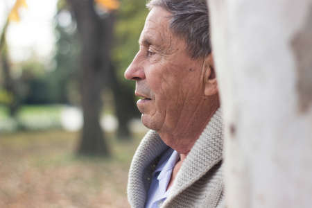 Portrait of happy senior man smiling, in the public park, outdoors.. Old man relaxing outdoors and looking up. Portrait of elderly man enjoying retirementの写真素材