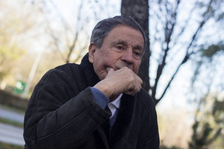 Portrait of a pensive senior man sitting on the bench, in the public park, outdoors. Old man relaxing outdoors and looking away. Portrait of senior man looking thoughtfulの写真素材