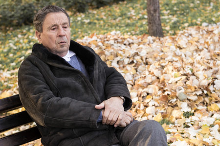 Portrait of a pensive senior man sitting on the bench, in the public park, outdoors. Old man...