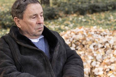 Portrait of a pensive senior man sitting on the bench, in the public park, outdoors. Old man relaxing outdoors and looking away. Portrait of elderly man enjoying retirementの写真素材