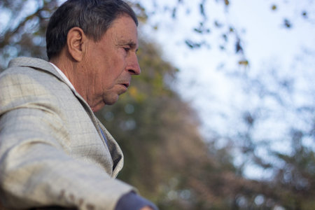 Portrait of a pensive senior man sitting on the bench, in the public park, outdoors. Old man...