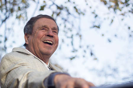 Portrait of happy senior man smiling, in the public park, outdoors. Old man relaxing outdoors and looking away. Portrait of elderly man enjoying retirementの写真素材