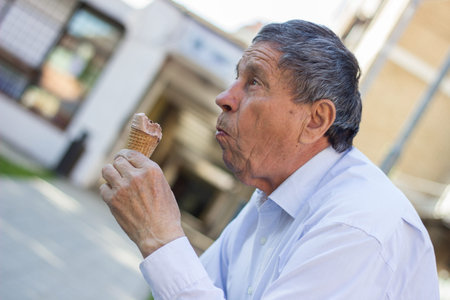 Modern and happy senior Man eating ice cream outdoor on a sunny dayの写真素材