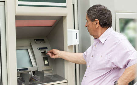 Senior man inserting credit card to ATM. Portrait of senior man with credit card, using a ATMの写真素材