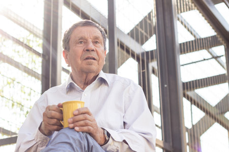 Senior man having his morning coffee outdoors. Day dreaming
