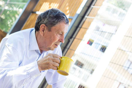Senior man having his morning coffee outdoors. Day dreamingの写真素材