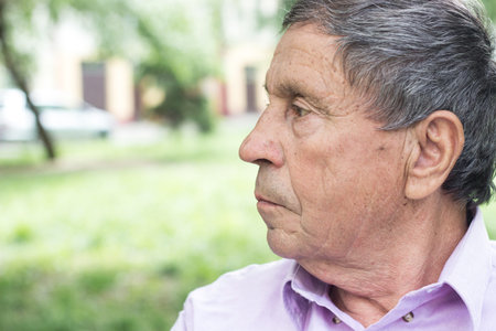 Portrait of a pensive senior man sitting on the bench, in the public park