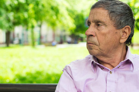 Portrait of a pensive senior man sitting on the bench, in the public park