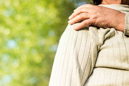 Senior woman with shoulder pain. Outdoors, sunlight, bokeh background.の写真素材