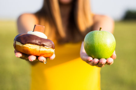 Woman choosing between healthy fruits and donut. Healthy lifestyle or nutrition conceptの写真素材