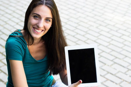Happy young woman with digital tablet in the city, looking at camera