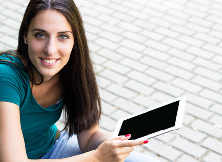 Happy young woman with digital tablet in the city, looking at camera