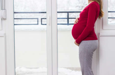 Pregnant beautiful woman holds hands on belly at home interiors. Resting at the homeの写真素材