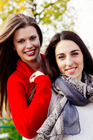 Two beautiful woman together enjoying the sunny autumn day, in the parkの写真素材