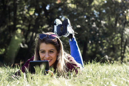Young smiling woman laying on grass and using tablet PC