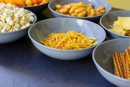 Salty snacks assortment shot on dark slate table. The picture includes potato chips, popcorn,...