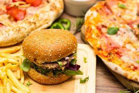 Pepperoni pizza and pizza Capricciosa with mozzarella cheese, ham, tomato sauce, salami, mushroom, pepper, spices and fresh basil. Hamburger with fries and fresh salad. On wooden tの写真素材