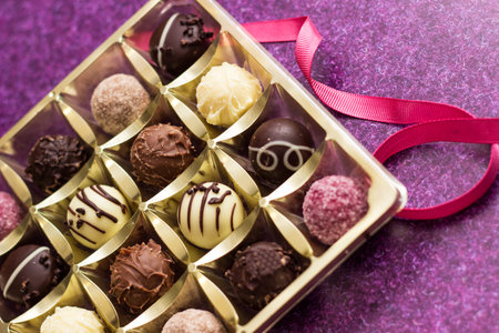 Golden box with delicious chocolate candies on purple table