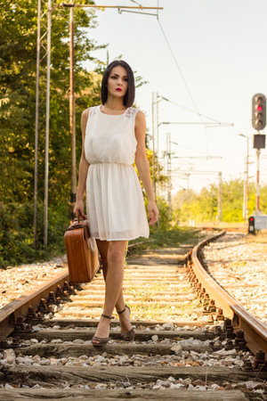 Woman walking on railroad tracks with suitcaseの写真素材