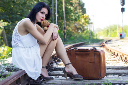 <p>Vintage woman on railroad tracks sitting on a suitcase and waiting for the train</p>の写真素材