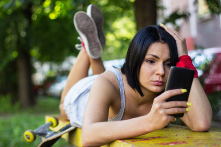 Hipster girl sitting on her skateboard and using smartphoneの写真素材