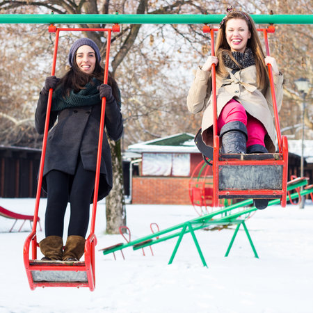 Two happy friends swinging on a swing, winterの写真素材