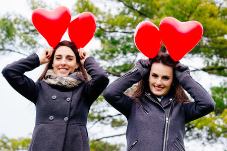 Two smiling girls holding hearts, portraitの写真素材