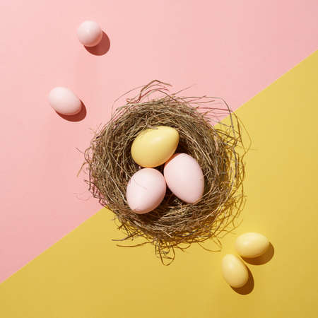 Creative composition of pastel pink and yellow colored Easter eggs in the nest. Minimal spring holiday concept. Natural sunlight and sharp shadows. Contemporary style.の写真素材