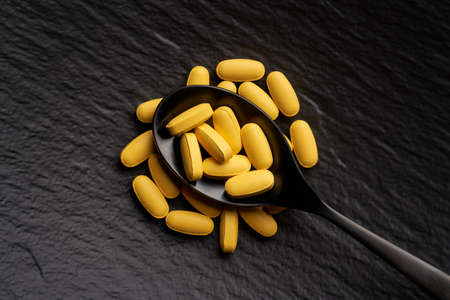 Close up pharmaceutical yellow pills on black stone background. Minimal modern concept, flat lay, top view.の写真素材