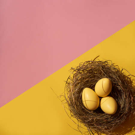 Creative composition of yellow colored Easter eggs in the nest on of pastel pink and yellow background. Minimal spring holiday concept. Contemporary style.の写真素材