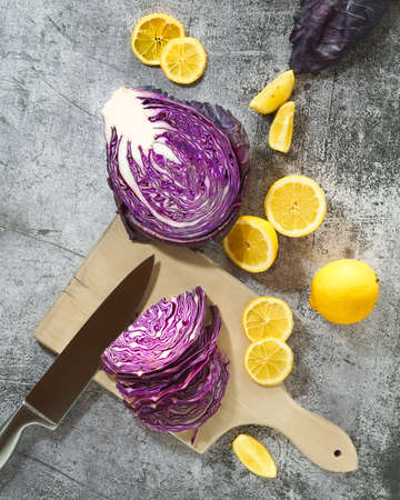 Raw red cabbage being sliced on wooden board with fresh lemons on grey surface. Colorful spring kitchen scene Top view.の写真素材