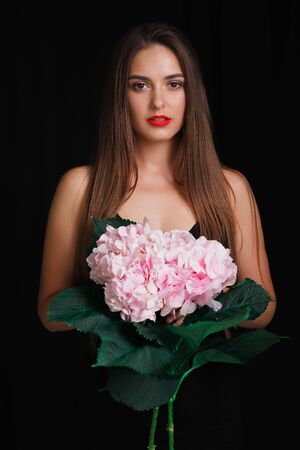 Brunette on a black background with a bouquet of large beautiful flowersの写真素材