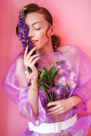 Beautiful brunette on a pink background. Decorated with flowersの写真素材