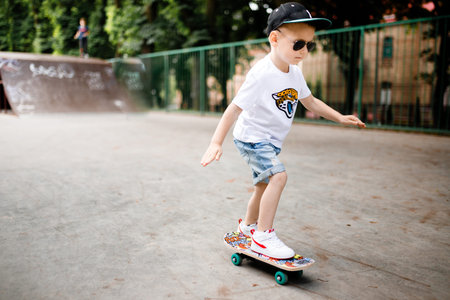 Boy with a skate in a skate park. A boy with glasses learns to skate in stylish clothes. A little extremeの写真素材