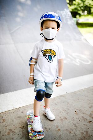 A boy with a skate in a mask, learning to skate, in full protection in quarantine.の写真素材
