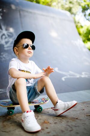 Boy with a skate in a skate park. The boy is sitting on a skateboard.の写真素材