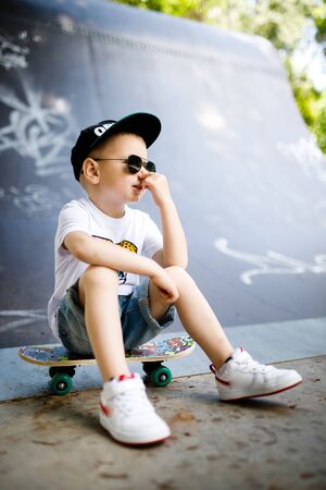 Boy with a skate in a skate park. The boy is sitting on a skateboard.の写真素材
