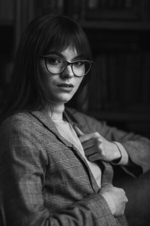 Beautiful dreamy girl in stylish sharp glasses. In the library.の写真素材