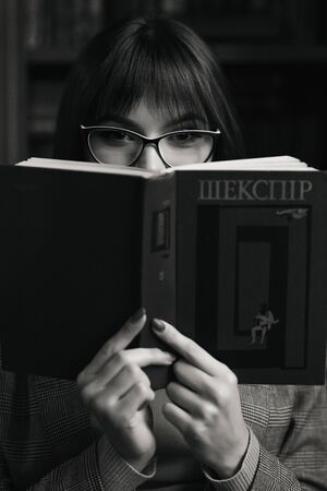 Beautiful dreamy girl in stylish sharp glasses, jacket and sweater. She covered herself with a book.の写真素材