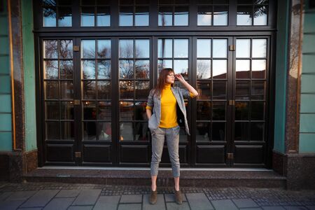 Beautiful dreamy girl in stylish sharp glasses. Near the shop windowの写真素材