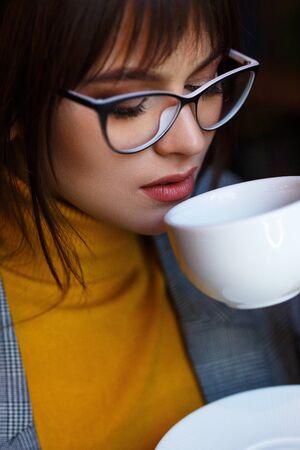 Beautiful dreamy girl in stylish sharp glasses. With a cup in his hands.の写真素材