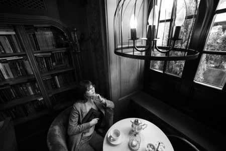 Beautiful dreamy girl in stylish sharp glasses. In the library.の写真素材