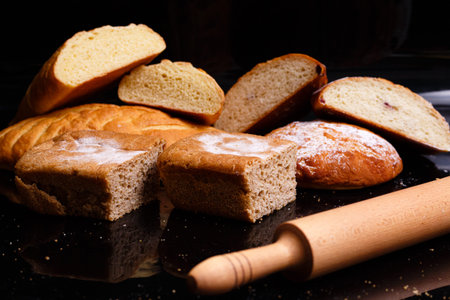 Baking on a black background with a rolling pin. Lots of pastries and bread.