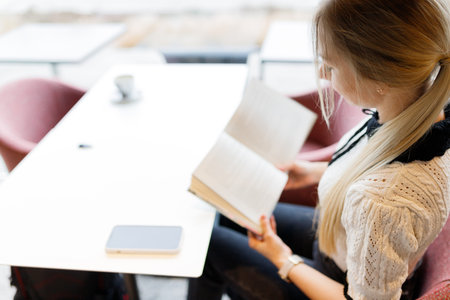 A young beautiful girl is reading a book in a cafeの写真素材