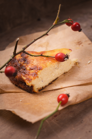 On a wooden table a piece of cheese cake , garnished with a sprig of wild rose , red berries .の写真素材