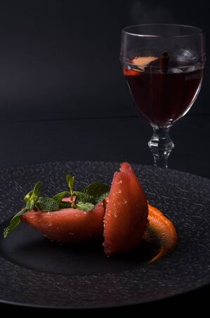 On a dark desert dish of pears with caramel and a glass of mulled wineの写真素材